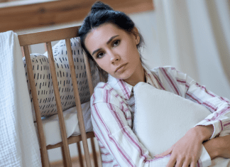 woman comforting self with pillow while leaning against a bed