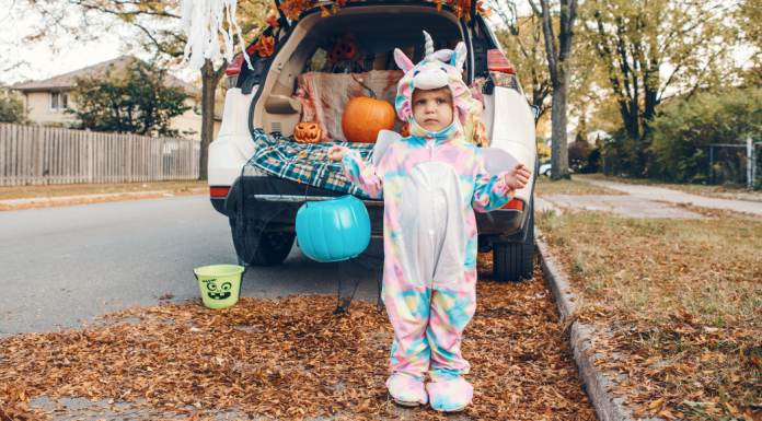Child in monster costume holding blue pumpkin to collect candy