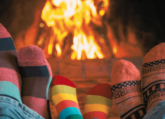three pairs of feet wearing cozy socks resting in front of a fire in a fireplace.