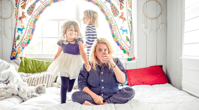 juggling motherhood featured image with a mom sitting on a bed with her kids