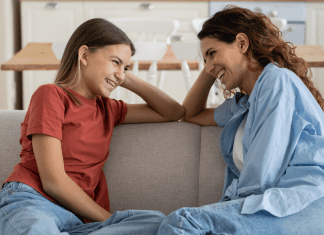 mom and teen daughter sitting on a couch talking to one another and smiling