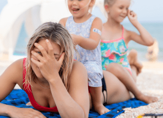 Mom laying on a towel at the beach while her kids sit on her back