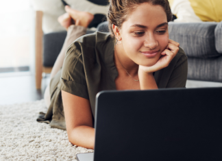 woman laying on family room floor looking at her laptop