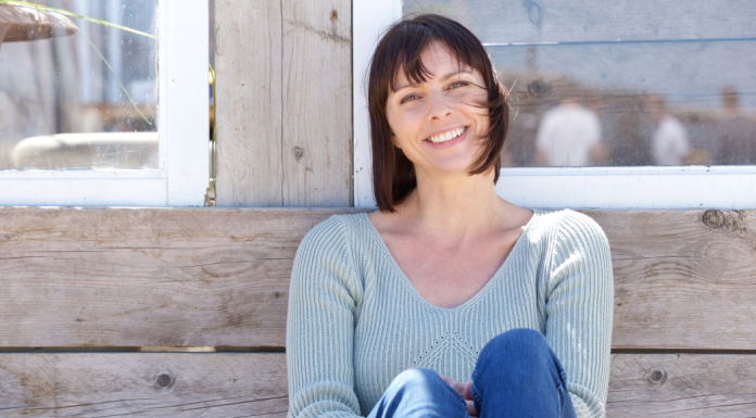 woman sitting against a wall outside smiling