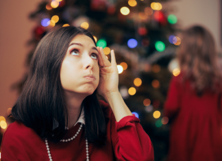 woman near christmas tree, stressed and holding her had to her head.