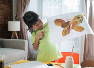 Preschool child holding up a paper collage with a butterfly made of leaves.