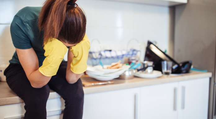 survival mode featured image with a woman wearing kitchen gloves sitting on a counter next to a pile of dirty dishes.